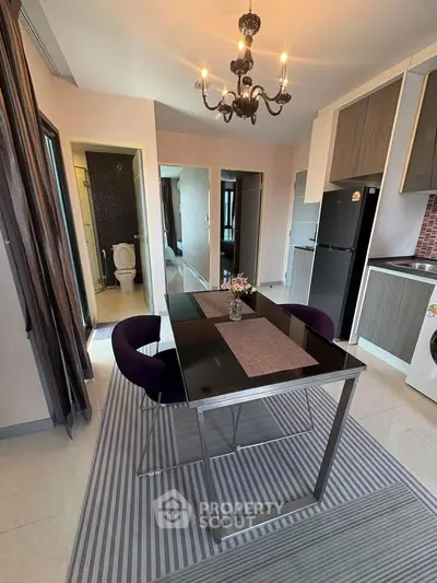Modern dining area with elegant chandelier and compact kitchen in stylish apartment.