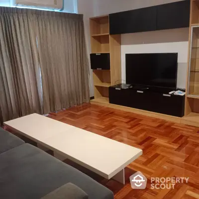 Spacious living room with polished parquet flooring, modern entertainment unit, and large windows draped with elegant curtains.