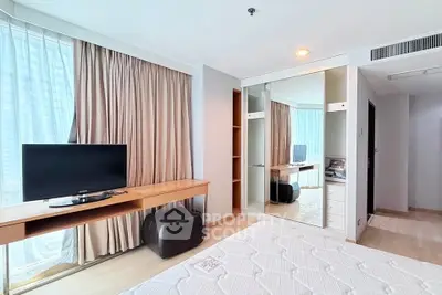Spacious bedroom with modern decor, featuring a large window, mirrored wardrobe, and sleek TV setup.