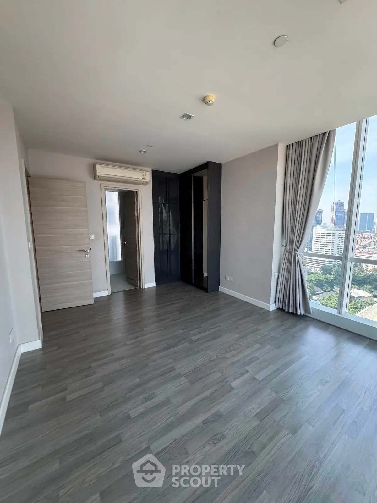 Spacious modern bedroom with city view and sleek flooring in high-rise apartment.