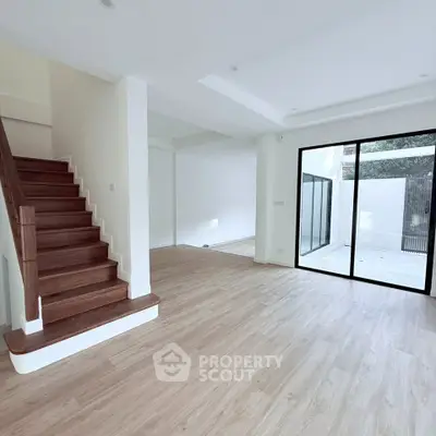 Spacious modern living room with wooden staircase and large glass doors opening to a patio.