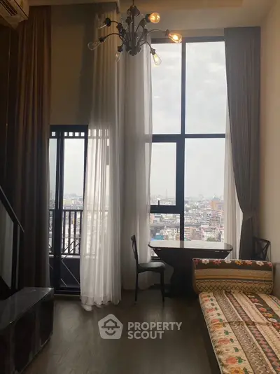 Spacious living room with high ceiling, large window offering city views, and access to a cozy balcony, perfect for urban living.