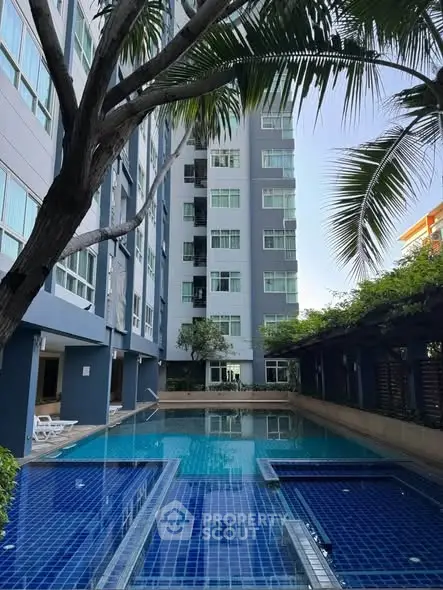 Luxurious apartment building with a stunning blue-tiled swimming pool and lush greenery.