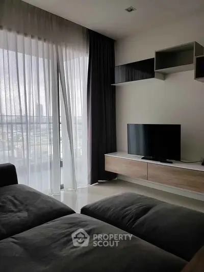 Modern living room with sleek furniture and large window offering city views.