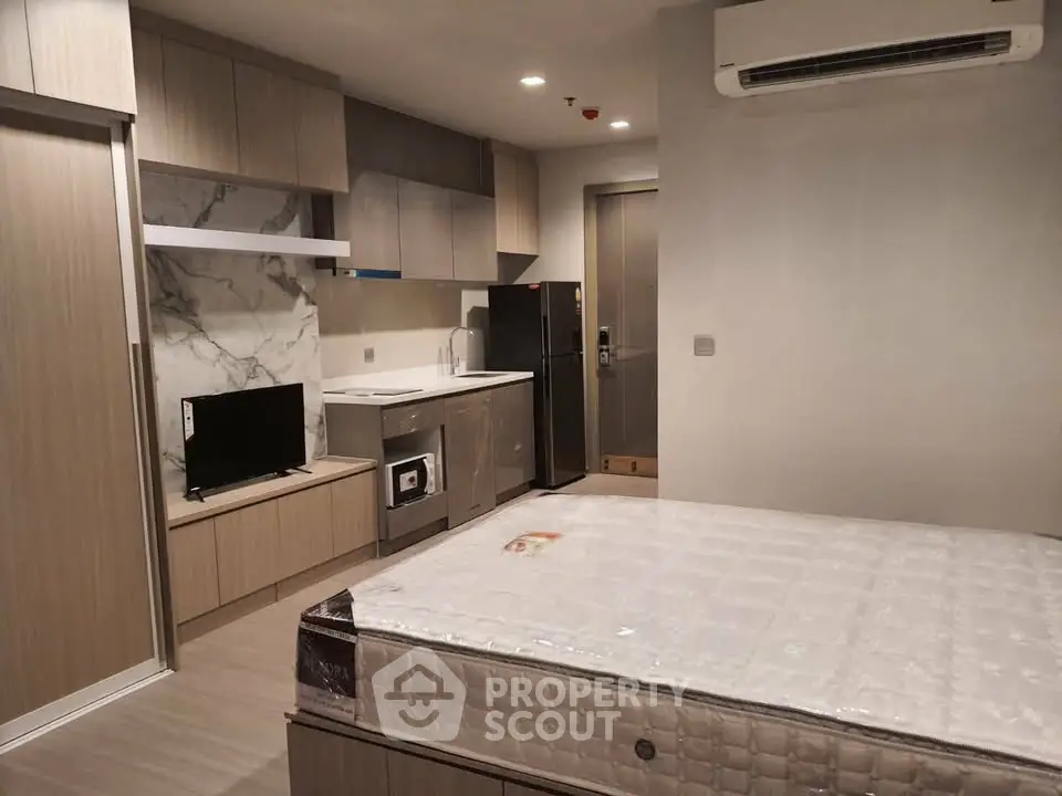Modern studio apartment with sleek kitchen and cozy living area, featuring built-in appliances and stylish decor.