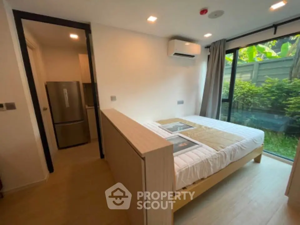 Modern bedroom with large window and garden view, featuring a cozy bed and air conditioning.