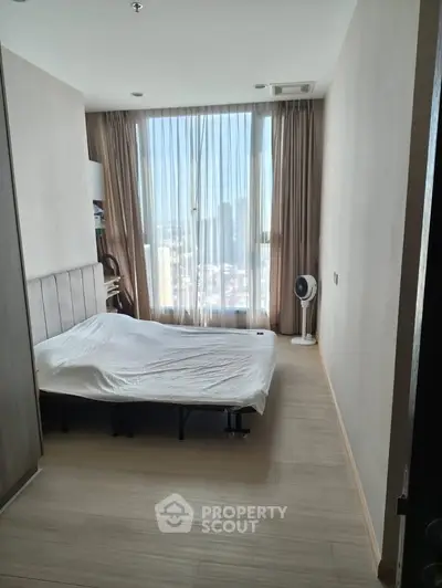 Cozy bedroom with large window offering city views, featuring a comfortable bed and modern decor.