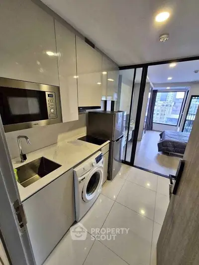 Modern kitchen with sleek appliances and view into a stylish bedroom in a contemporary apartment.