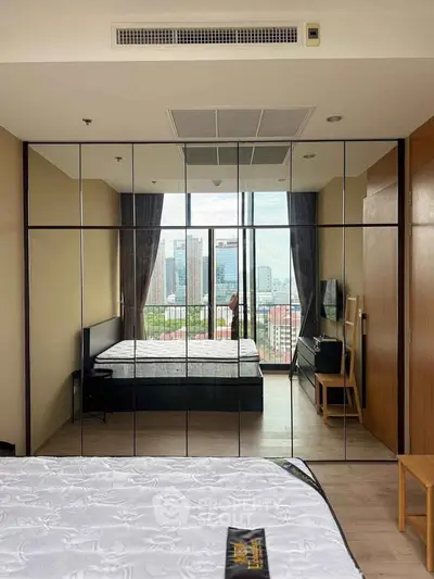 Modern bedroom with mirrored wardrobe and city view balcony in luxury apartment.