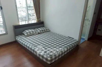 Cozy bedroom with checkered bedding and wooden flooring, featuring ample natural light from large windows.