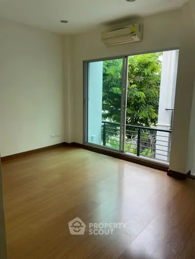 Spacious room with wooden flooring and large window overlooking greenery, perfect for a serene living space.