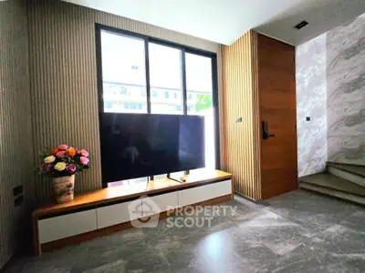 Modern living room with large TV, stylish decor, and natural light.