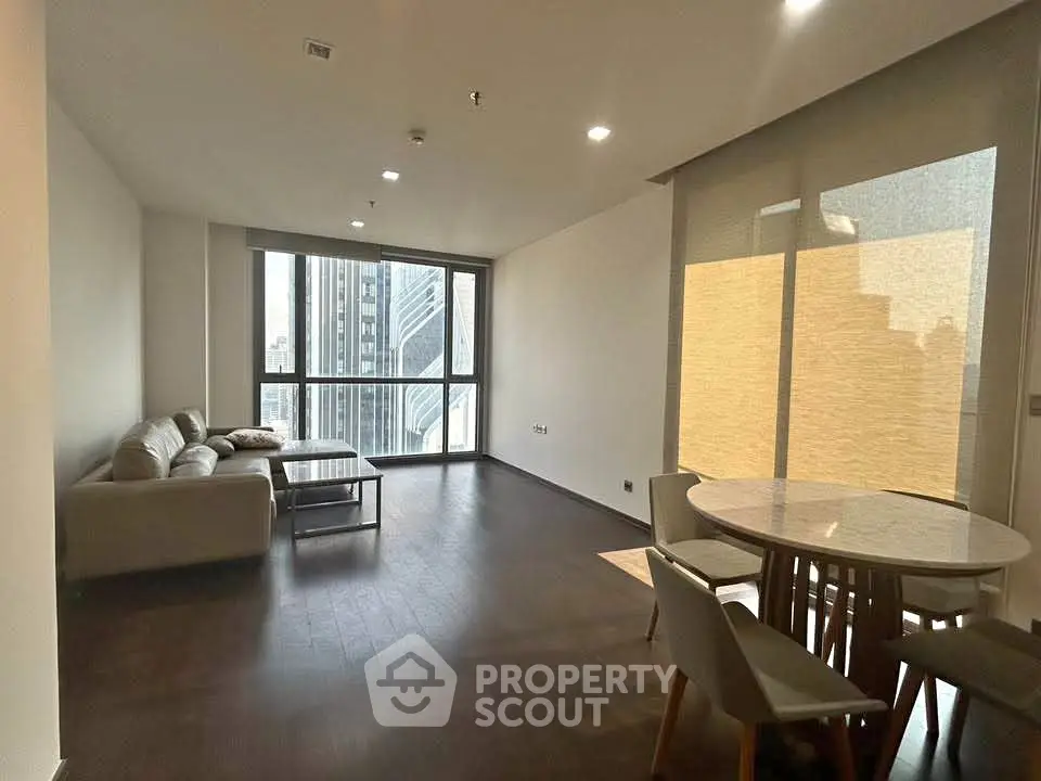 Spacious modern living room with city view, featuring elegant furniture and large windows.
