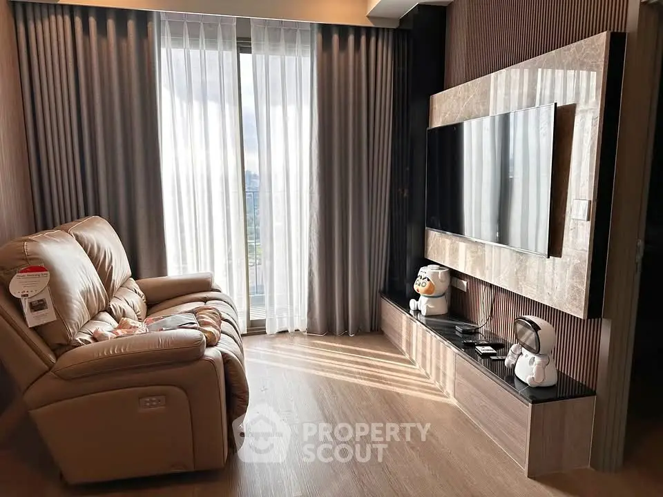 Modern living room with large TV and comfortable recliner chair, featuring floor-to-ceiling windows.