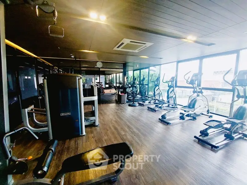 Spacious modern gym with state-of-the-art equipment and large windows offering natural light.