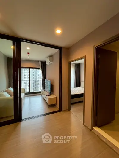 Modern apartment interior with spacious living room and bedroom, featuring large windows and wooden flooring.
