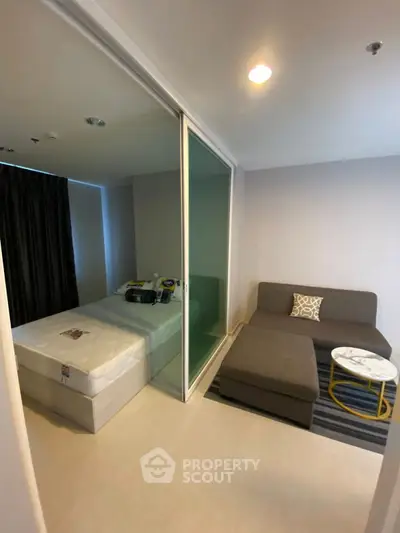 Modern studio apartment with cozy living area and bed separated by glass partition.