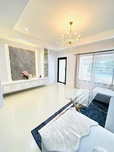 Elegant living room with chandelier and modern decor, featuring a cozy sofa and glass coffee table.