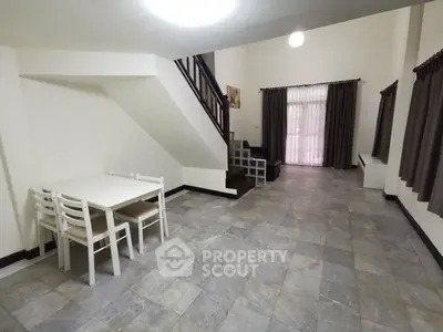 Spacious living room with elegant tile flooring, large windows with dark curtains, and a cozy staircase leading to the upper level, perfect for family gatherings.