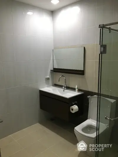 Modern bathroom with sleek fixtures and glass shower door in contemporary apartment.