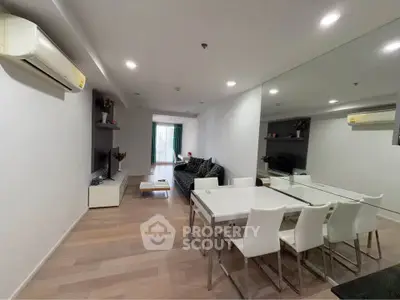 Spacious modern living room with dining area and mirrored wall, featuring sleek furniture and wooden flooring.