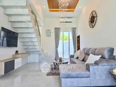 Modern living room with stylish staircase and plush gray sofa in a bright, airy space.