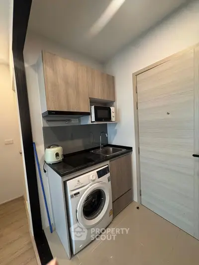 Compact modern kitchen with washing machine and microwave in a cozy apartment.