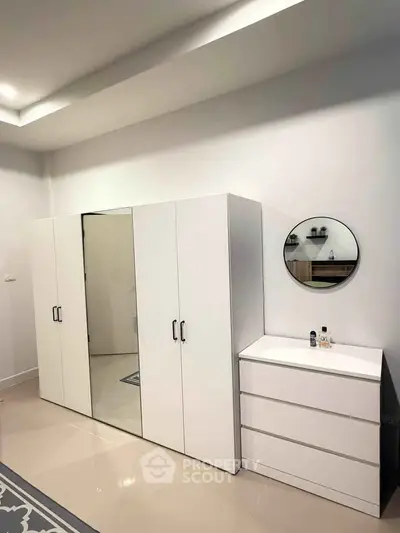 Modern bedroom with sleek white wardrobe and dresser, featuring a stylish round mirror.