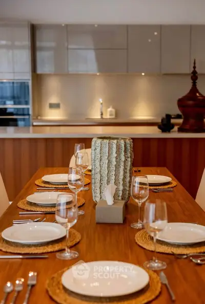 Elegant dining area with modern kitchen in open layout, featuring stylish table setting and warm lighting.