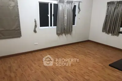 Spacious empty room with wooden flooring and large windows, perfect for customization.