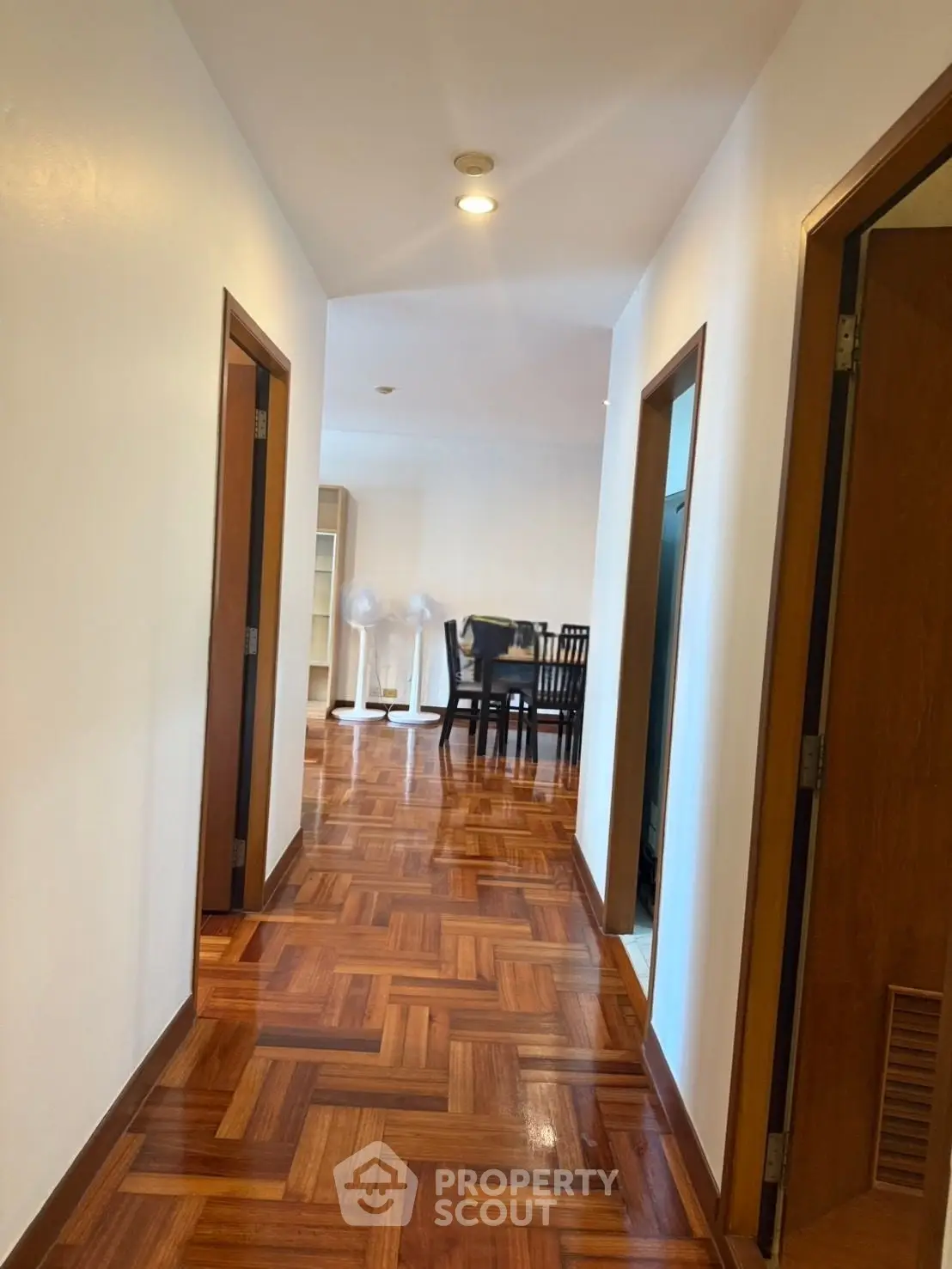 Spacious apartment hallway leading to a dining area with elegant wooden flooring.
