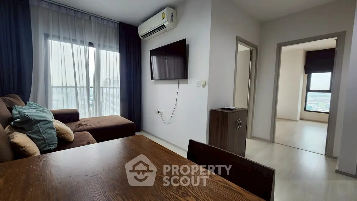 Modern living room with cozy sofa, wall-mounted TV, and large window with city view.