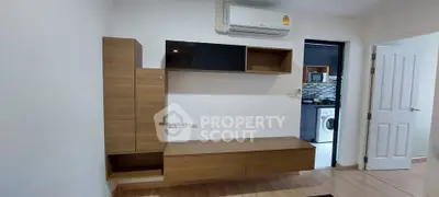 Modern living room with built-in wooden cabinets and view into kitchen with washing machine.