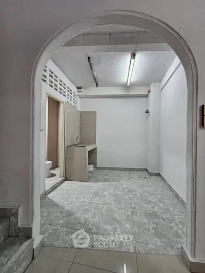 Spacious interior with tiled flooring and archway, featuring a small kitchenette and bathroom.