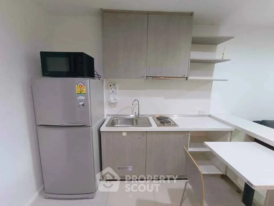 Modern compact kitchen with fridge, microwave, and sleek cabinetry in a cozy apartment.