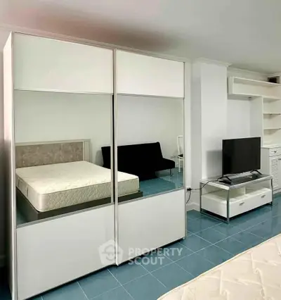 Modern studio apartment with sleek furniture and blue tile flooring, featuring a cozy bed and entertainment area.