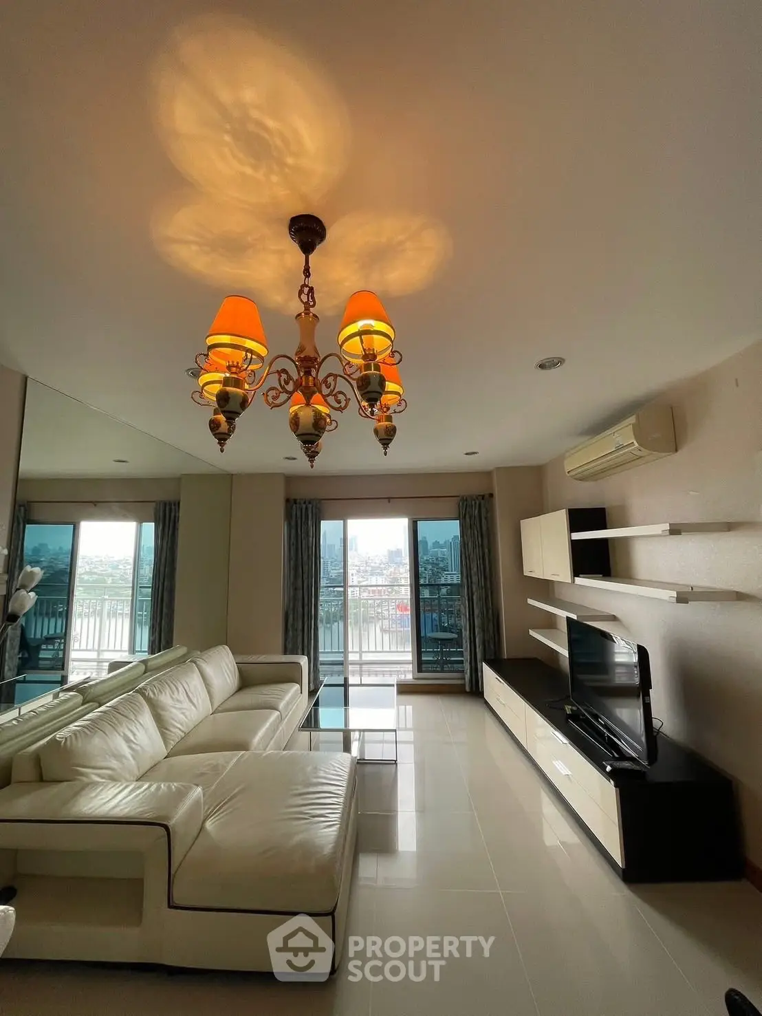 Spacious living room with elegant chandelier and city view balcony.