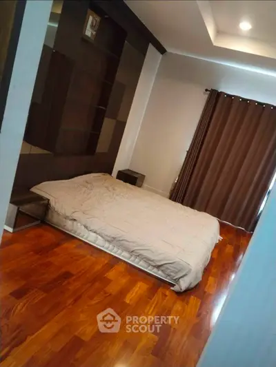 Spacious bedroom with wooden flooring and modern decor, featuring a cozy bed and elegant curtains.