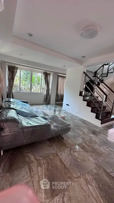 Spacious living room with modern staircase and large windows offering natural light.