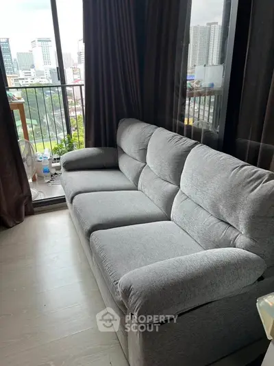 Modern living room with plush gray sofa and city view from balcony, perfect for urban living.