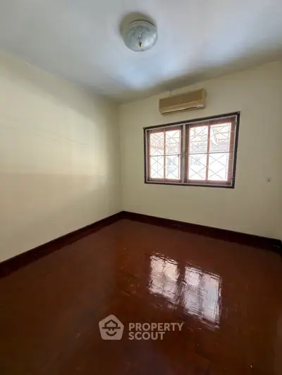 Spacious empty room with polished wooden floors and large window, ideal for customization.