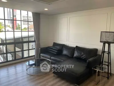 Modern living room with black leather sofa and large windows offering city views.