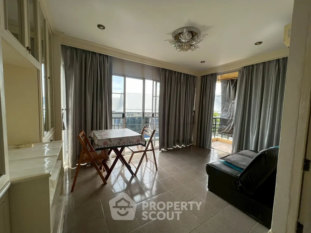 Bright living room with large windows and balcony access, featuring cozy seating and dining area.