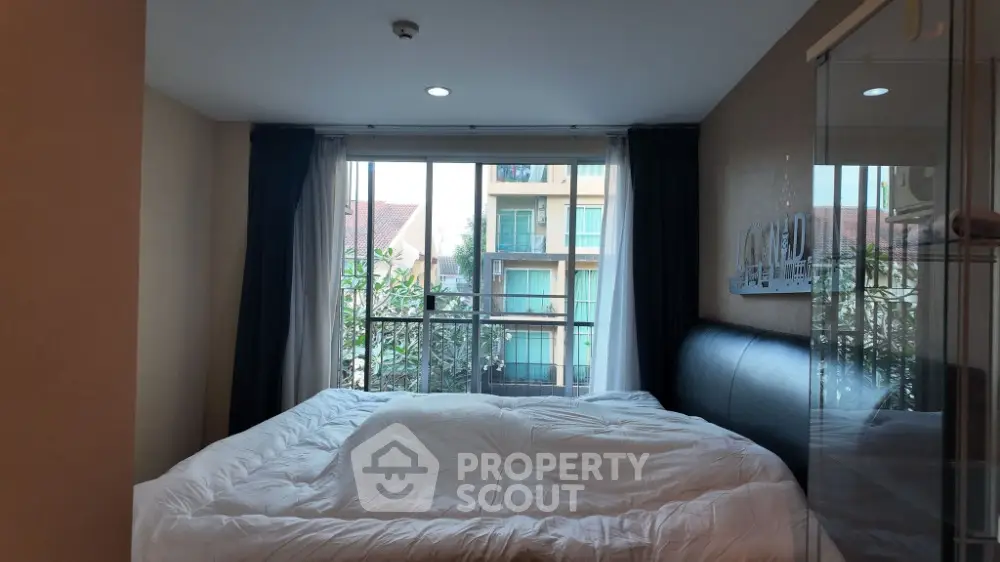Cozy bedroom with large window offering natural light and a view of the building exterior.
