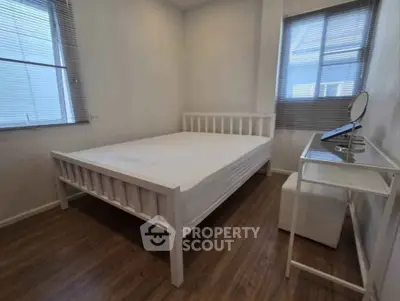 Cozy bedroom with wooden flooring and ample natural light from two windows.