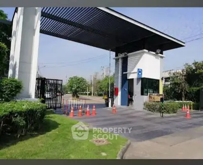 Modern gated entrance with security booth and lush greenery