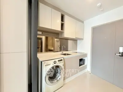 Modern kitchen with washing machine and sleek cabinetry in a compact apartment.