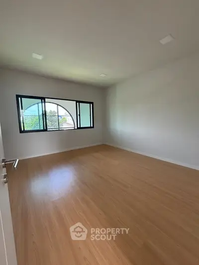 Spacious empty room with wooden flooring and large window, perfect for customization.
