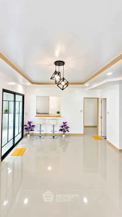 Spacious modern living room with elegant lighting and glossy tiled floors, featuring a breakfast bar and sliding glass doors.