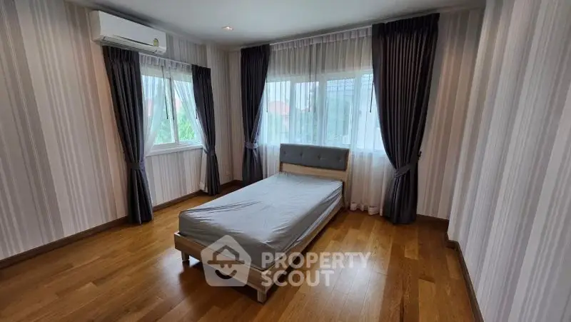 Spacious bedroom with wooden flooring and large windows for natural light.